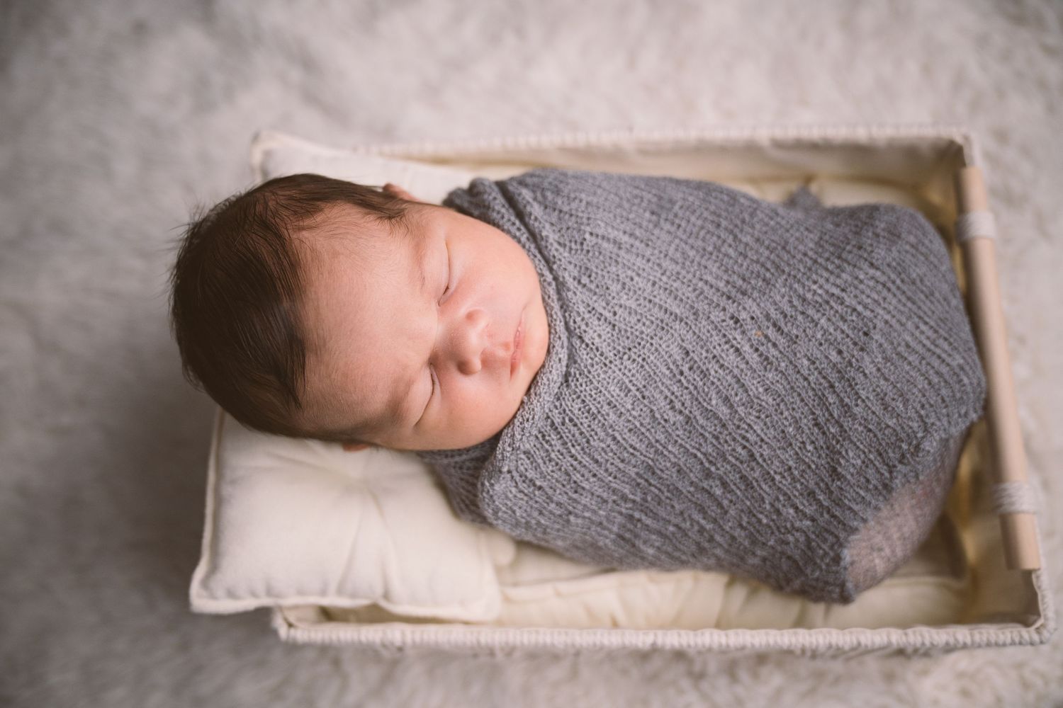 Peaceful sleeping baby wrapped in soft gray swaddle on white pillow.