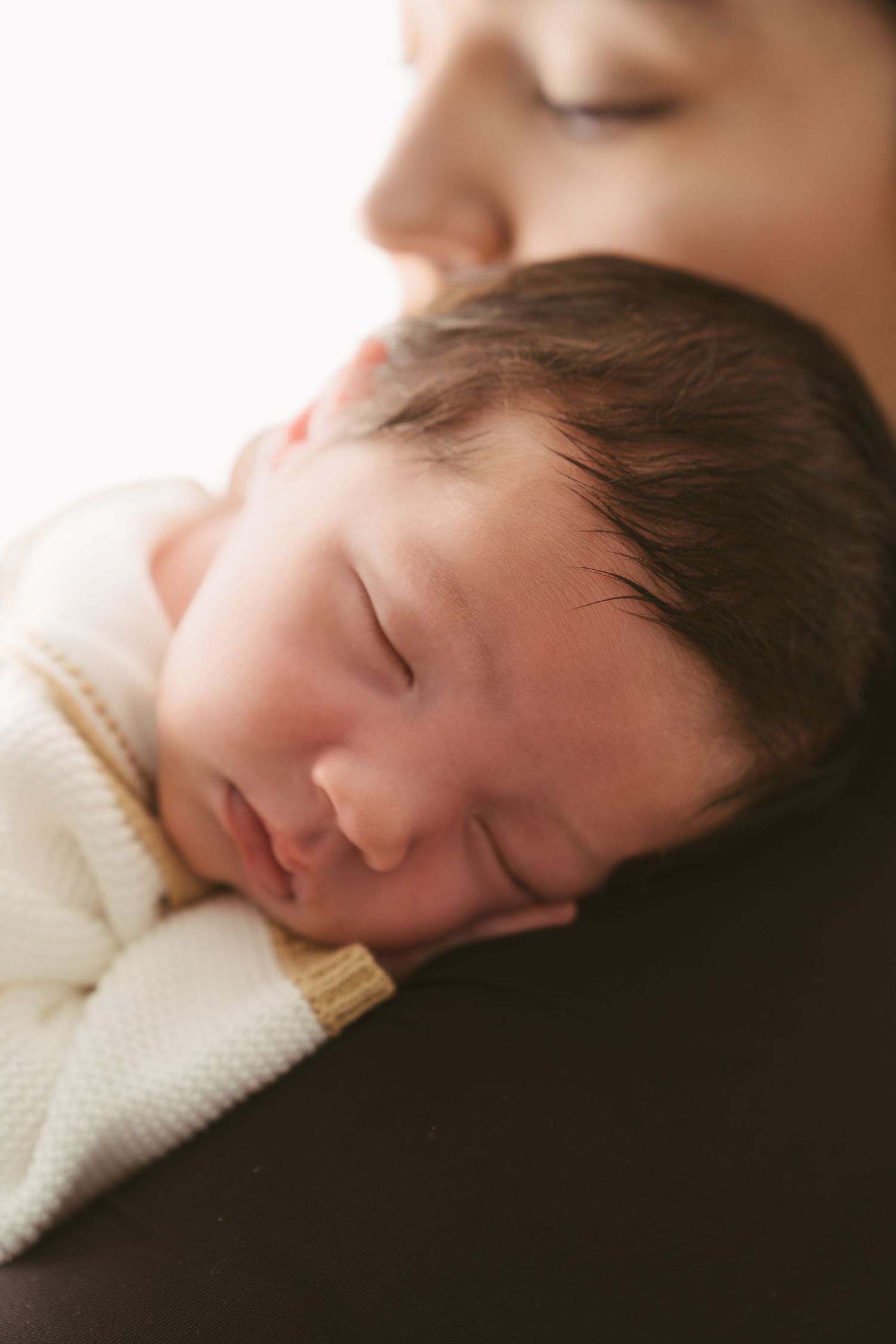 Sleeping baby in white sweater nestled against caregiver in intimate portrait.