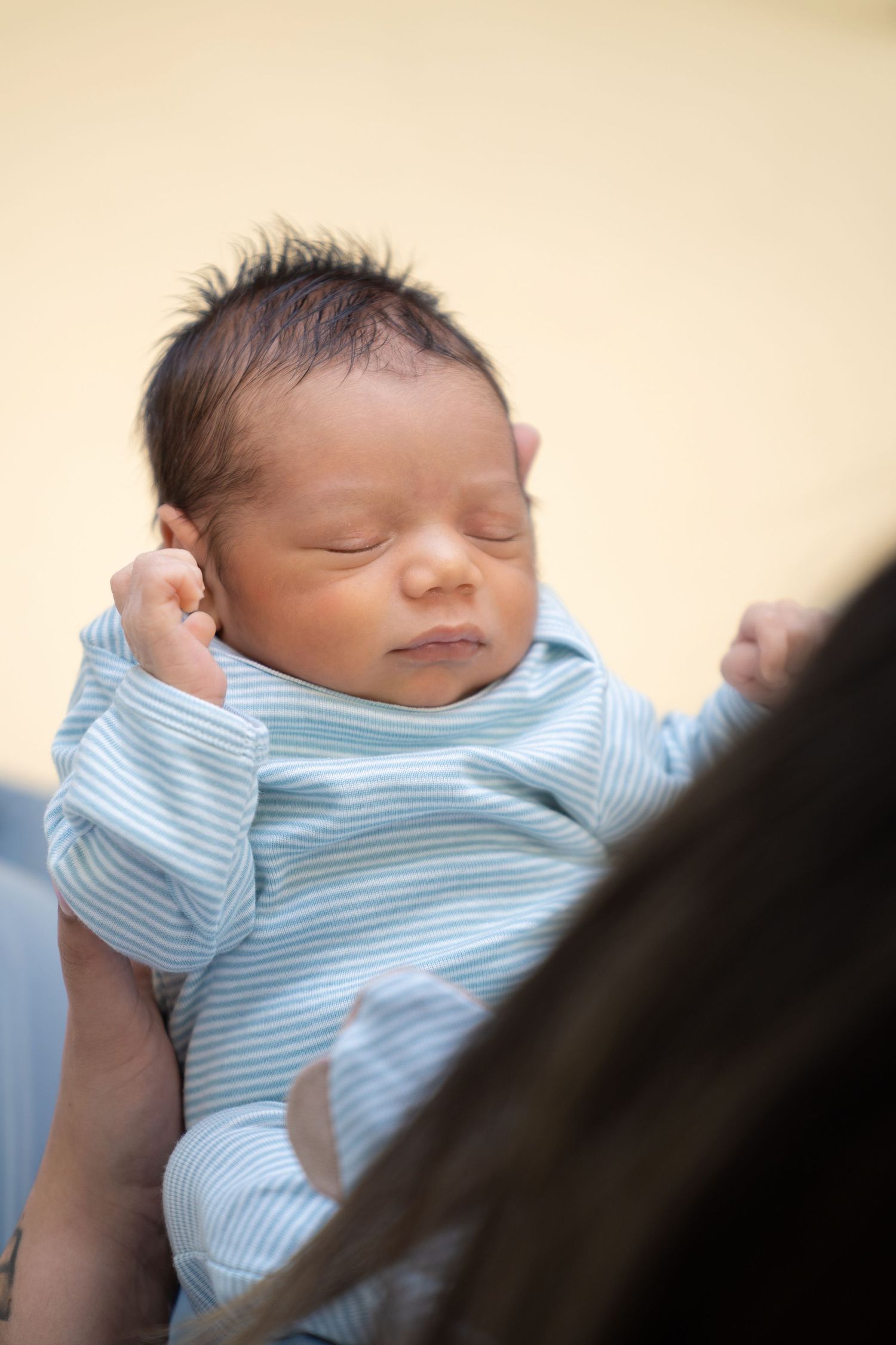Sleeping newborn wearing striped onesie in gentle natural light.