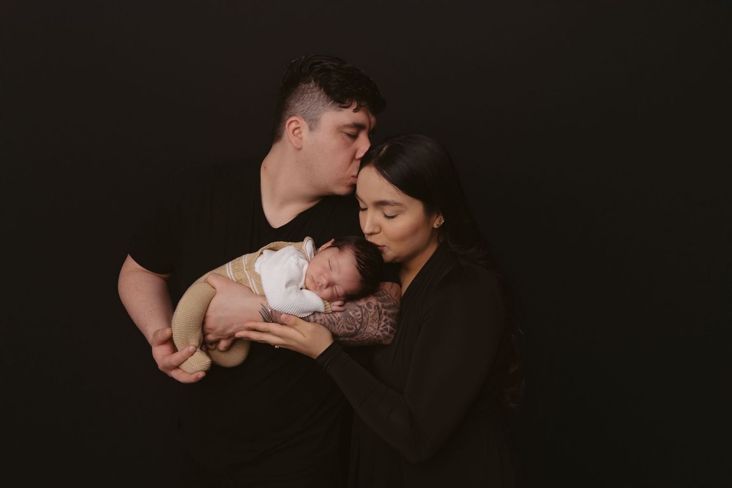Intimate family moment with sleeping baby against dark backdrop.