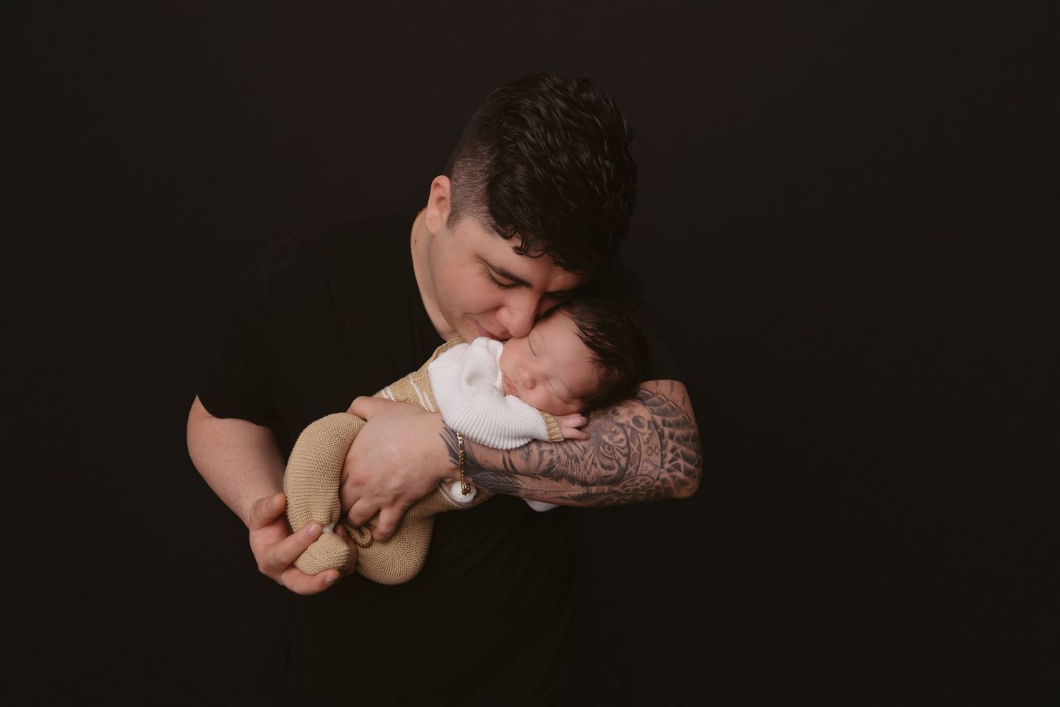 Intimate portrait of parent cradling sleeping baby against dark background.