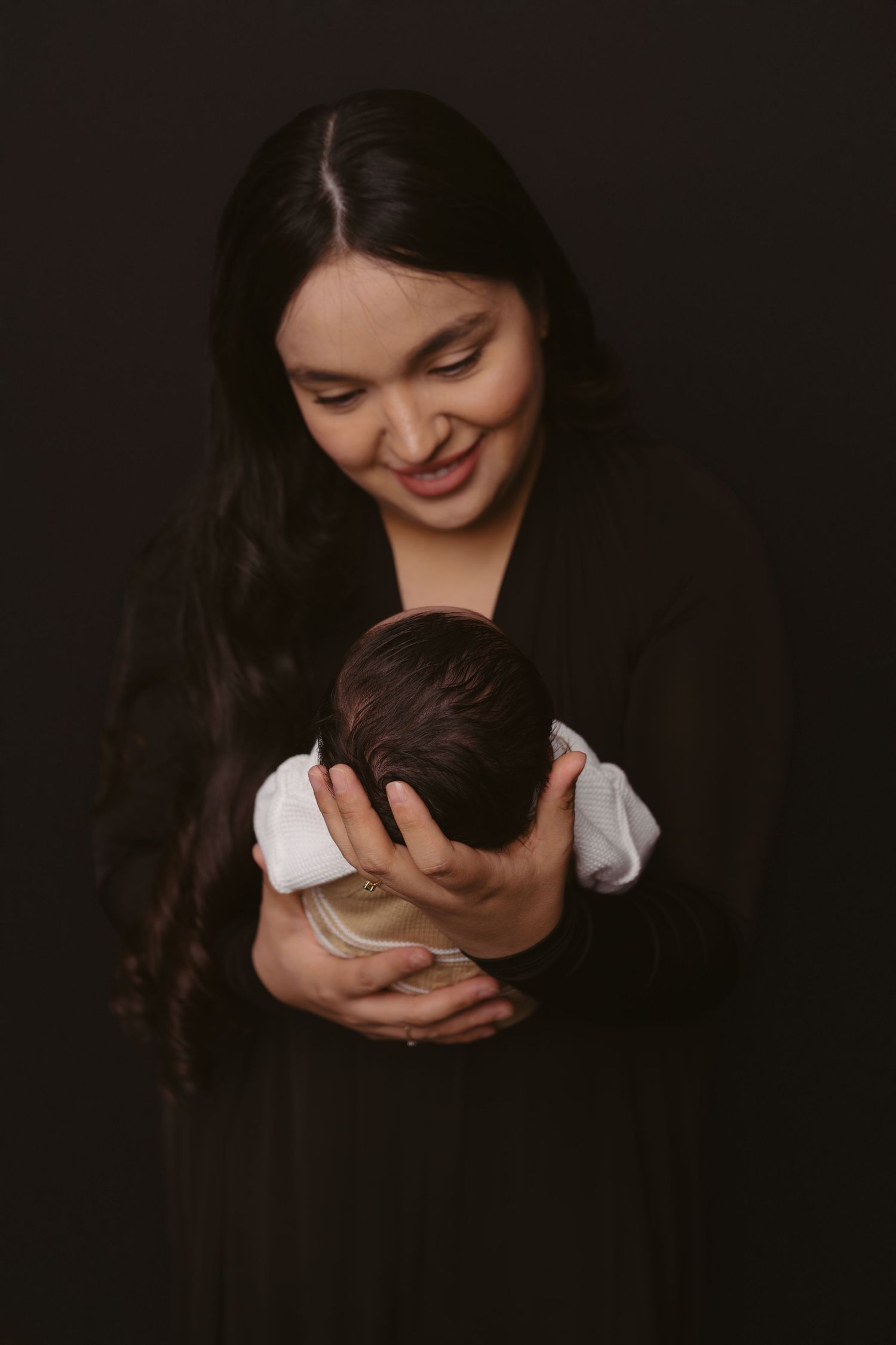 Parent gazing lovingly at sleeping baby against dark background.