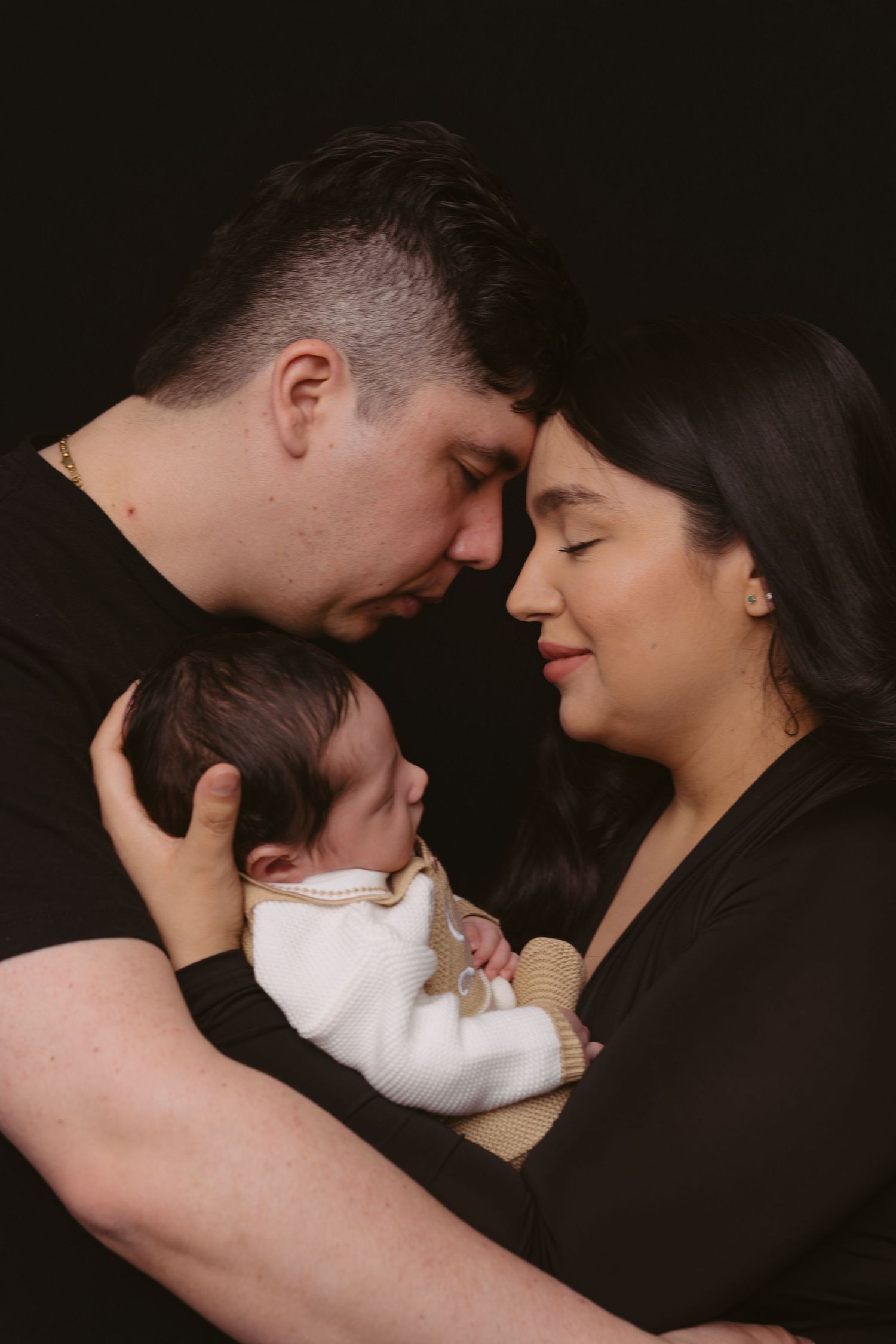 Intimate family portrait with sleeping baby against dark background.