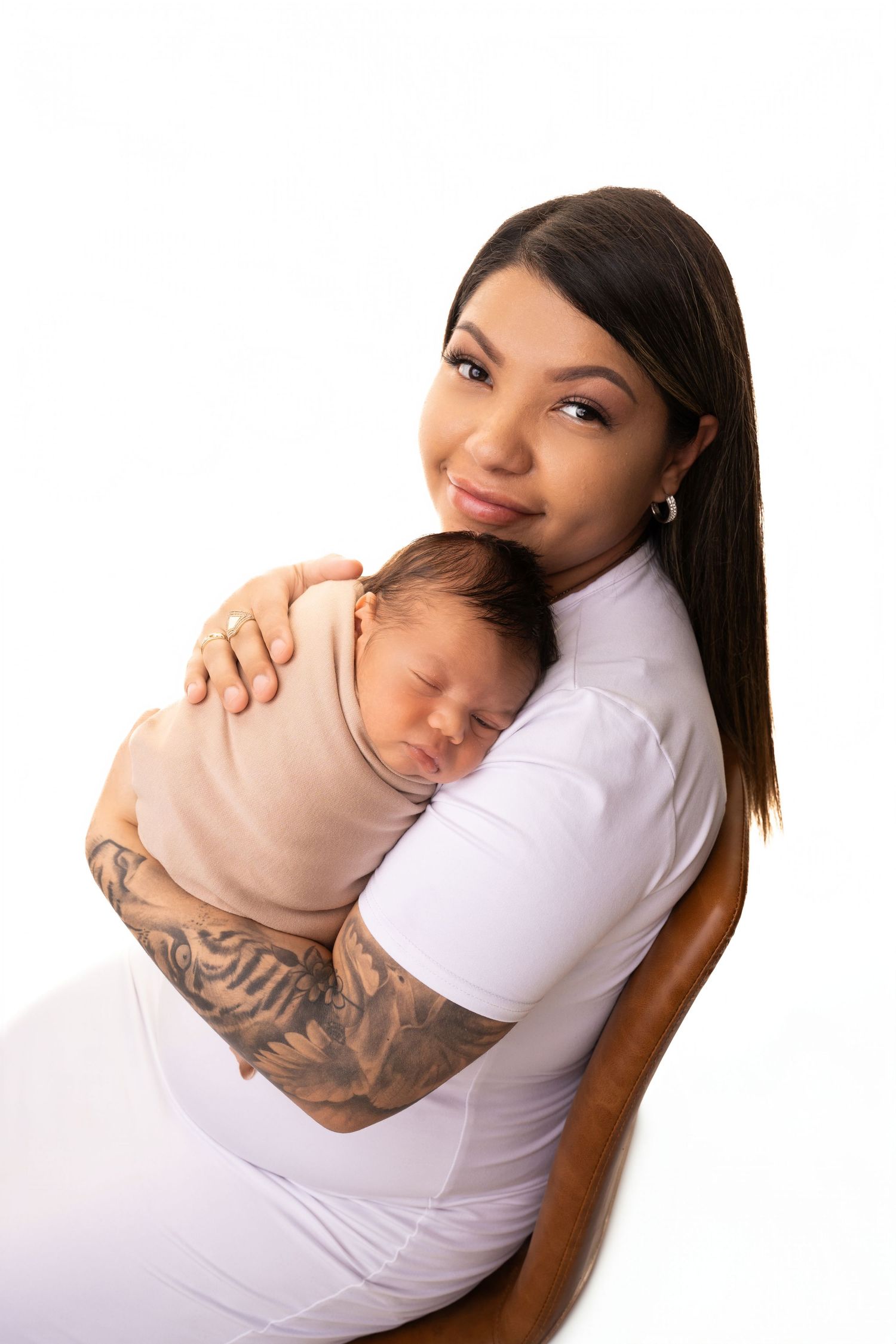 Parent in white shirt holding sleeping newborn against clean white background.
