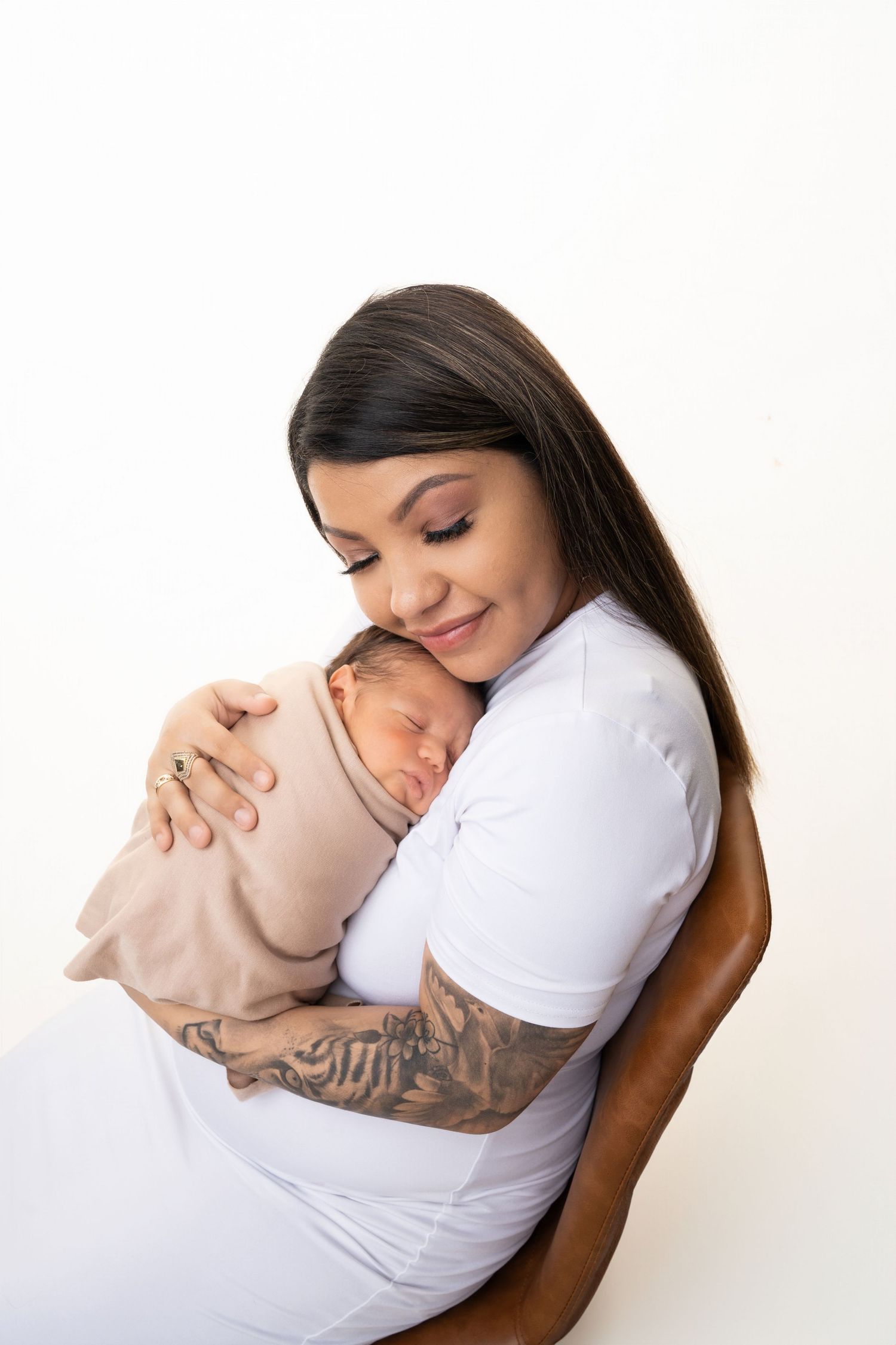 A tender moment between parent and newborn baby in white against a light background.