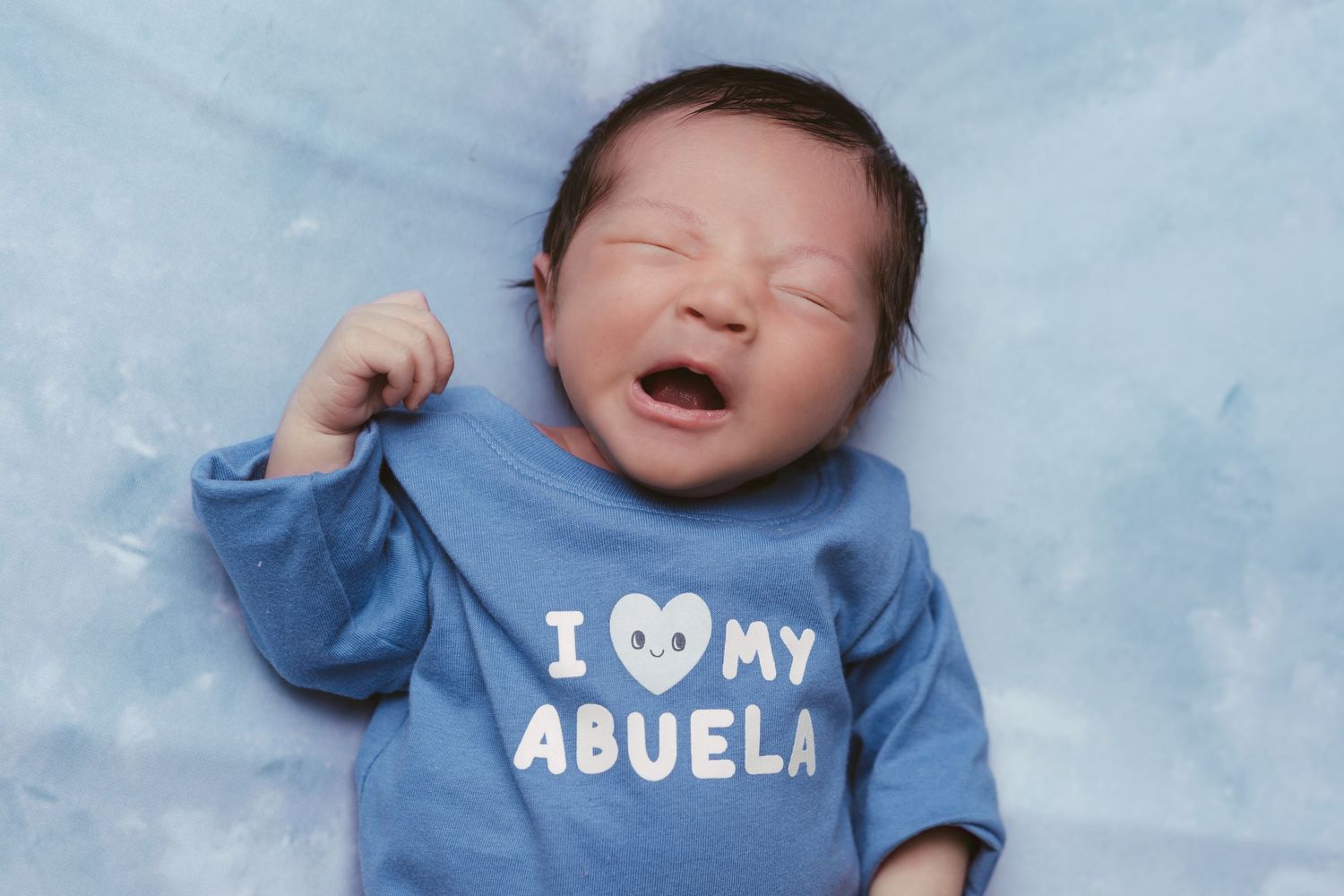 Baby wearing blue clothing with text photographed against light blue background.