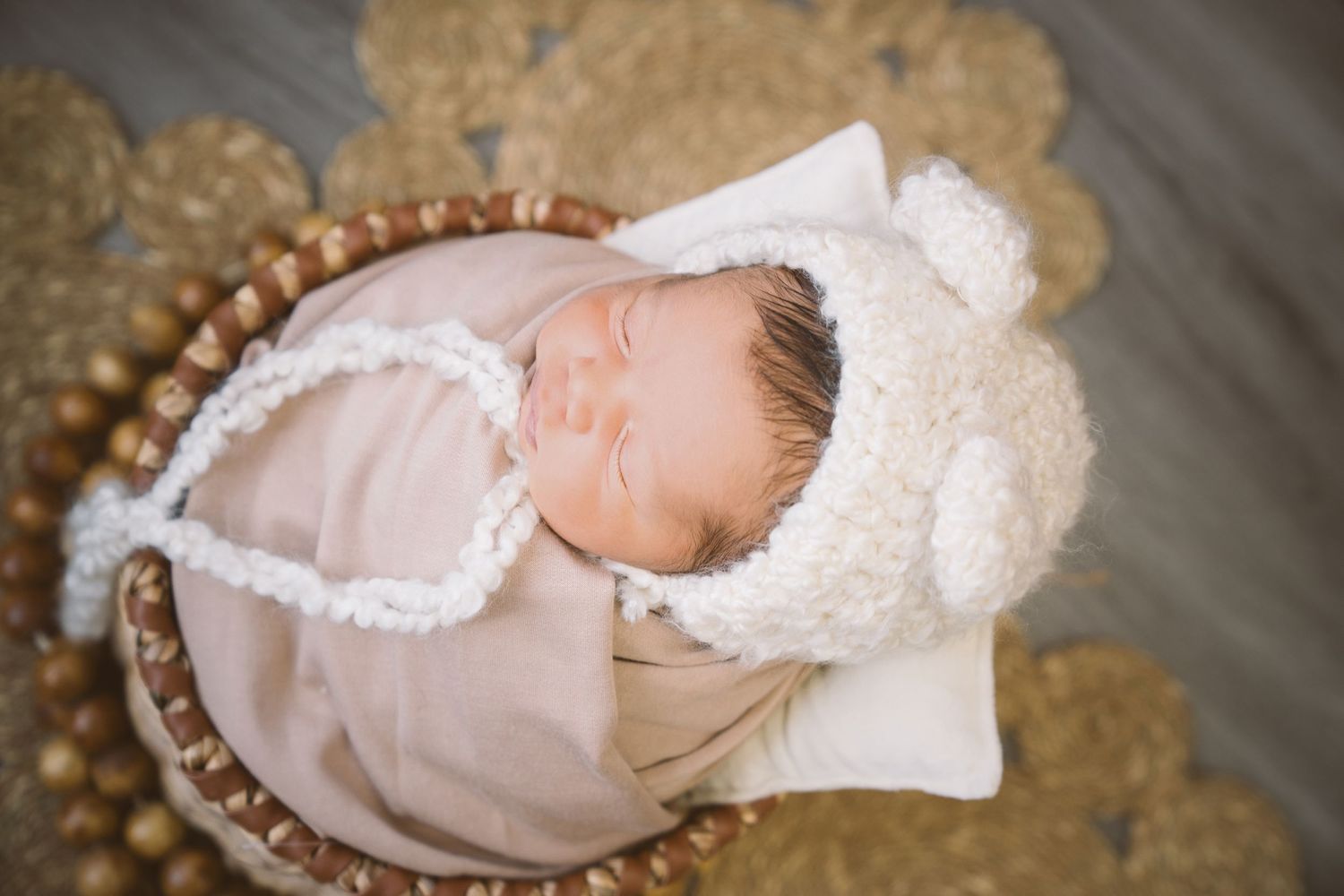 Peaceful newborn baby sleeping in a cozy basket wearing a white bear hat.