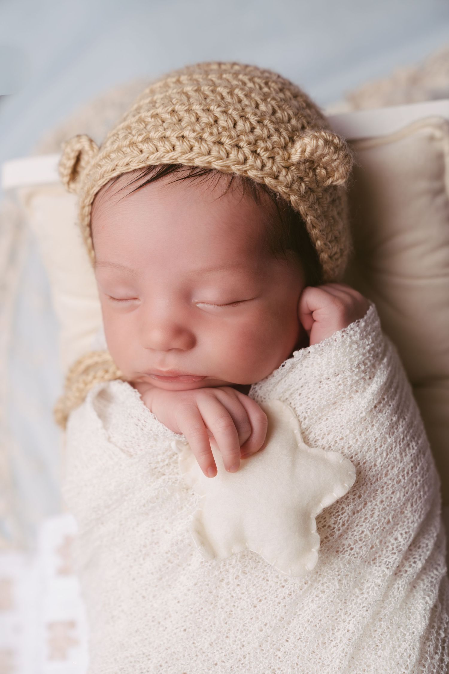 Sleeping newborn wearing knit hat wrapped in white blanket.