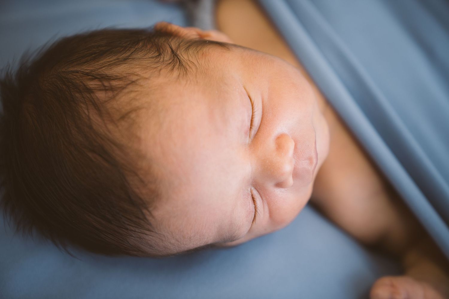 Peaceful sleeping newborn baby photographed in soft blue lighting.