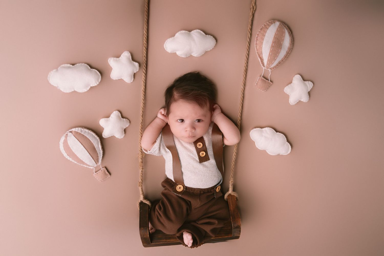 Adorable newborn photography setup with white clouds and stars against a soft pink background.