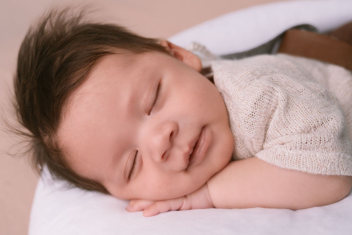 A peaceful sleeping baby in white clothing rests on soft bedding.