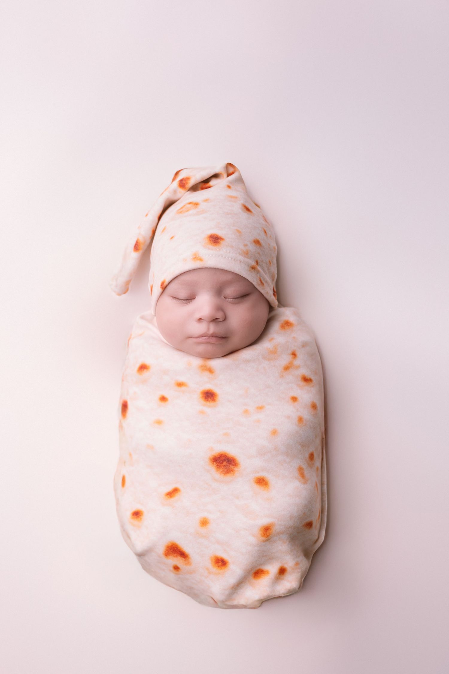Baby swaddled in white and orange floral wrap against white background.