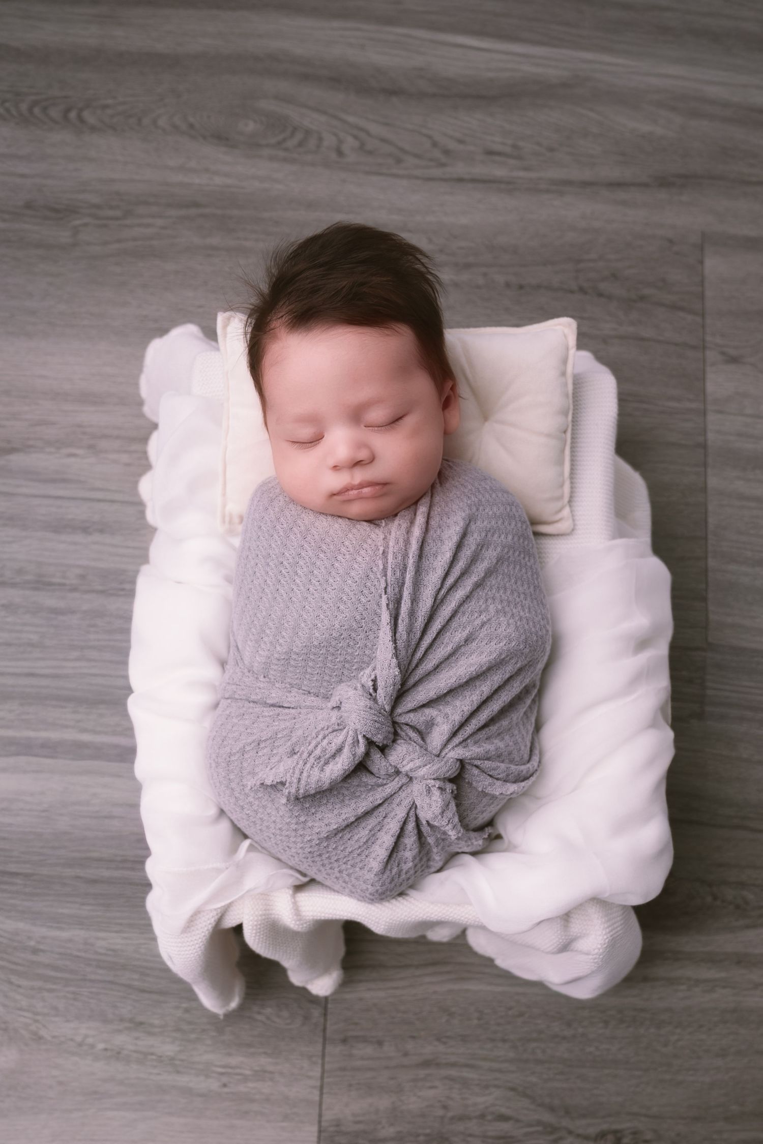Newborn wrapped in gray knit blanket sleeping on white cloud-shaped pillow.