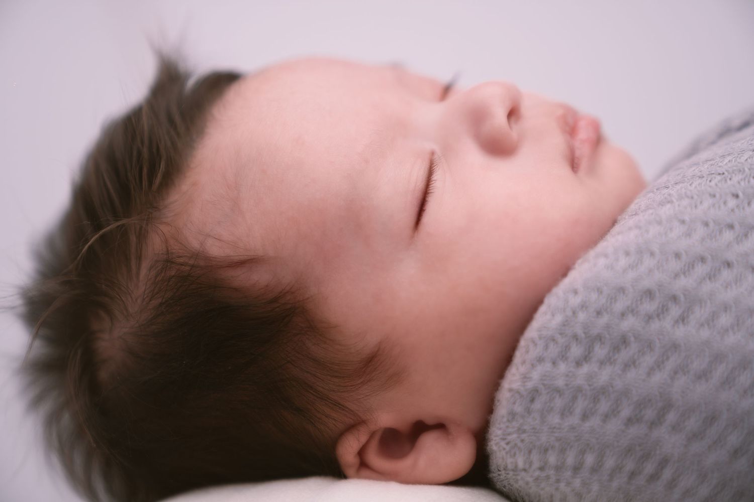 Peaceful sleeping baby resting on soft gray bedding in gentle natural light.