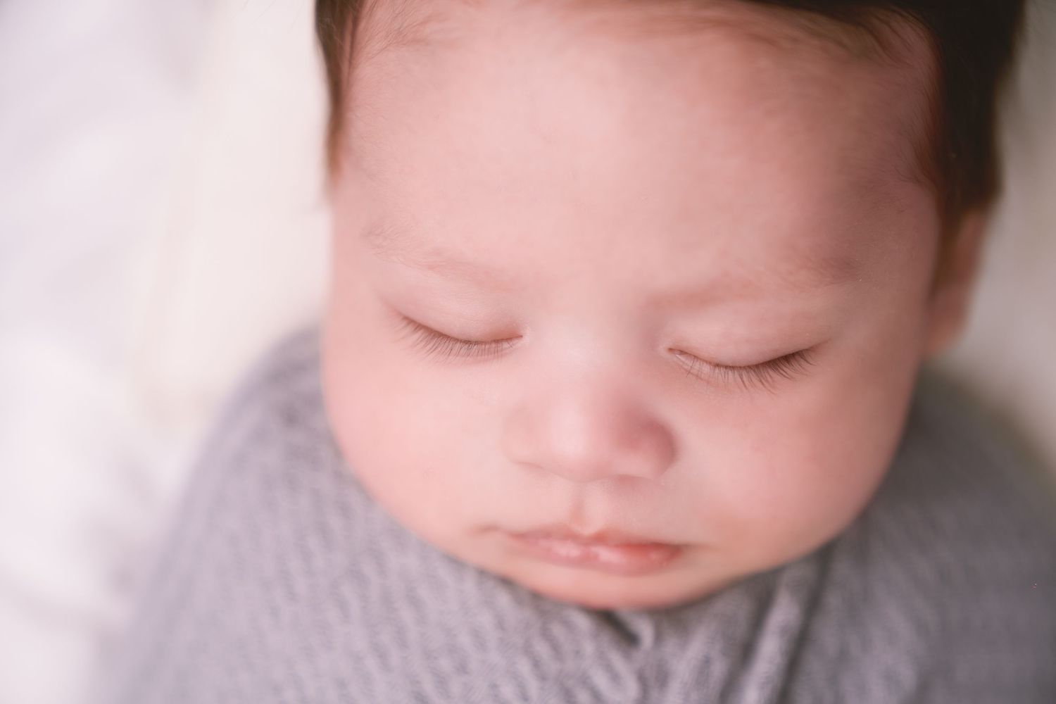 Close-up of a sleeping infant wearing a gray knit outfit against white bedding.