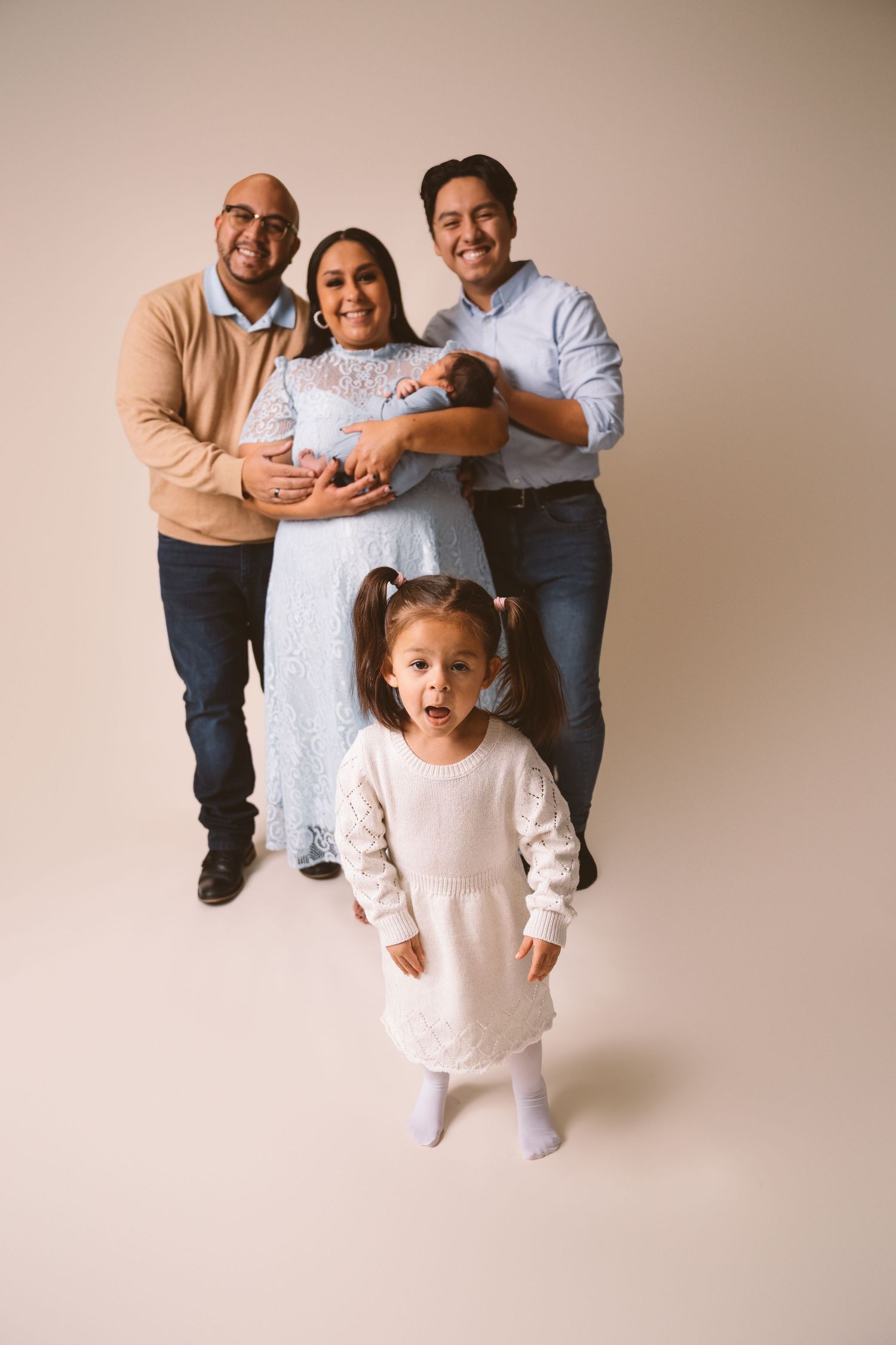 A multi-generational family portrait with a newborn baby and excited young child.