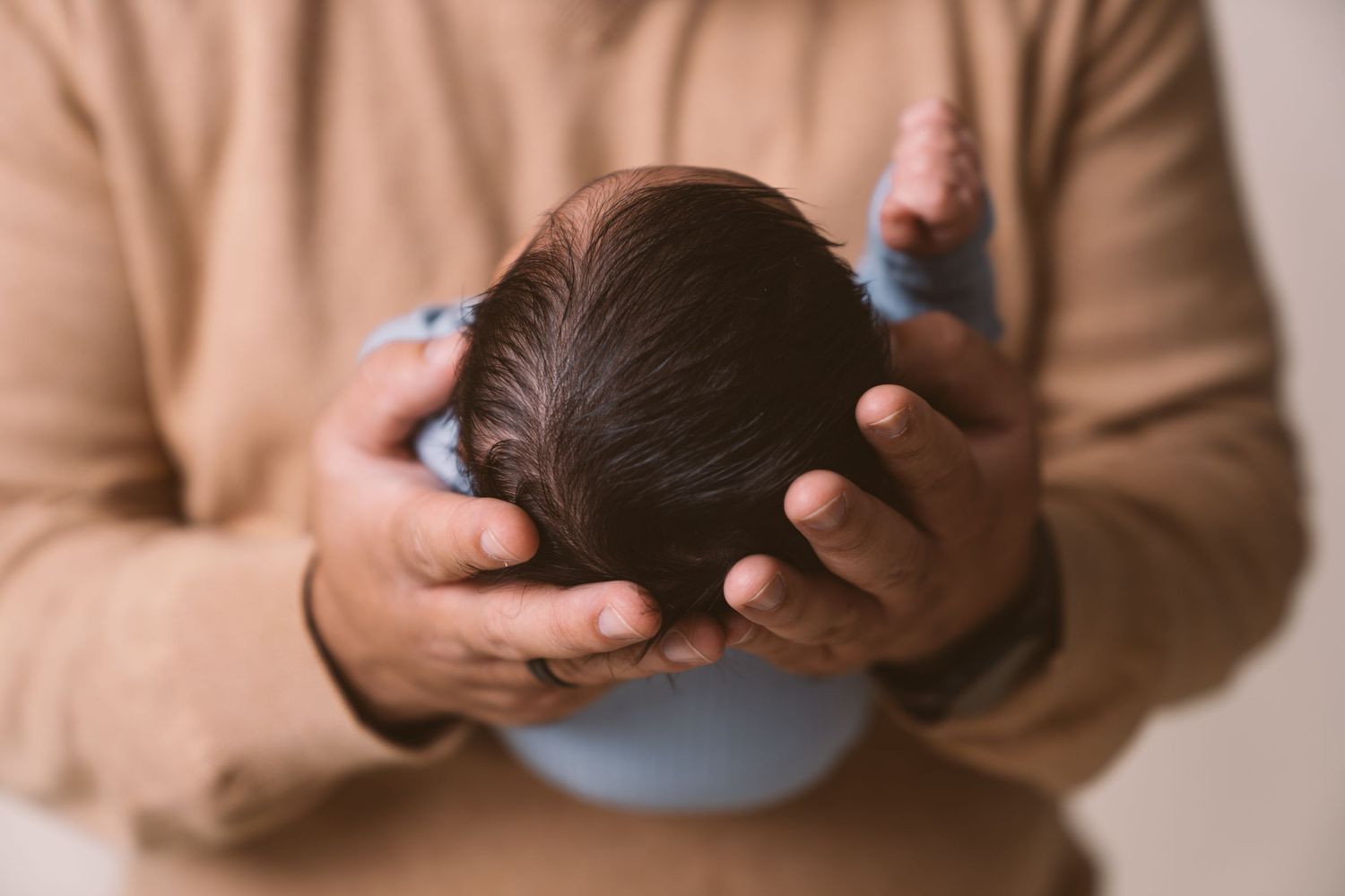 Gentle hands cradling a newborn baby's head in warm lighting.
