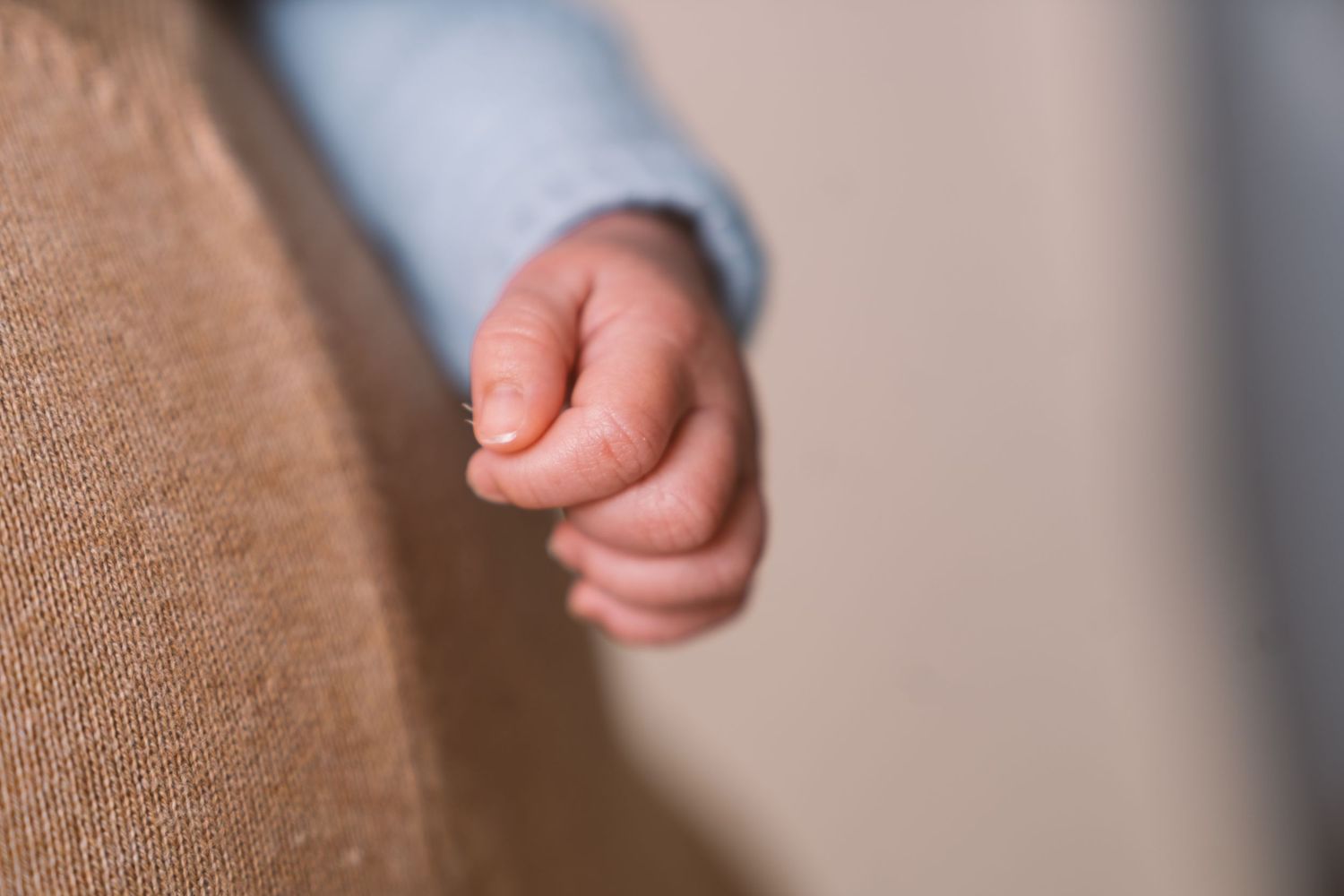 Close-up of tiny newborn baby hand against beige fabric.
