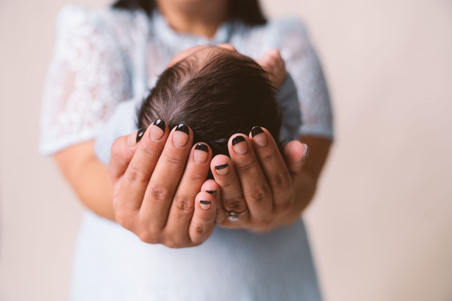 Tender moment with a sleeping newborn baby being held against white lace.