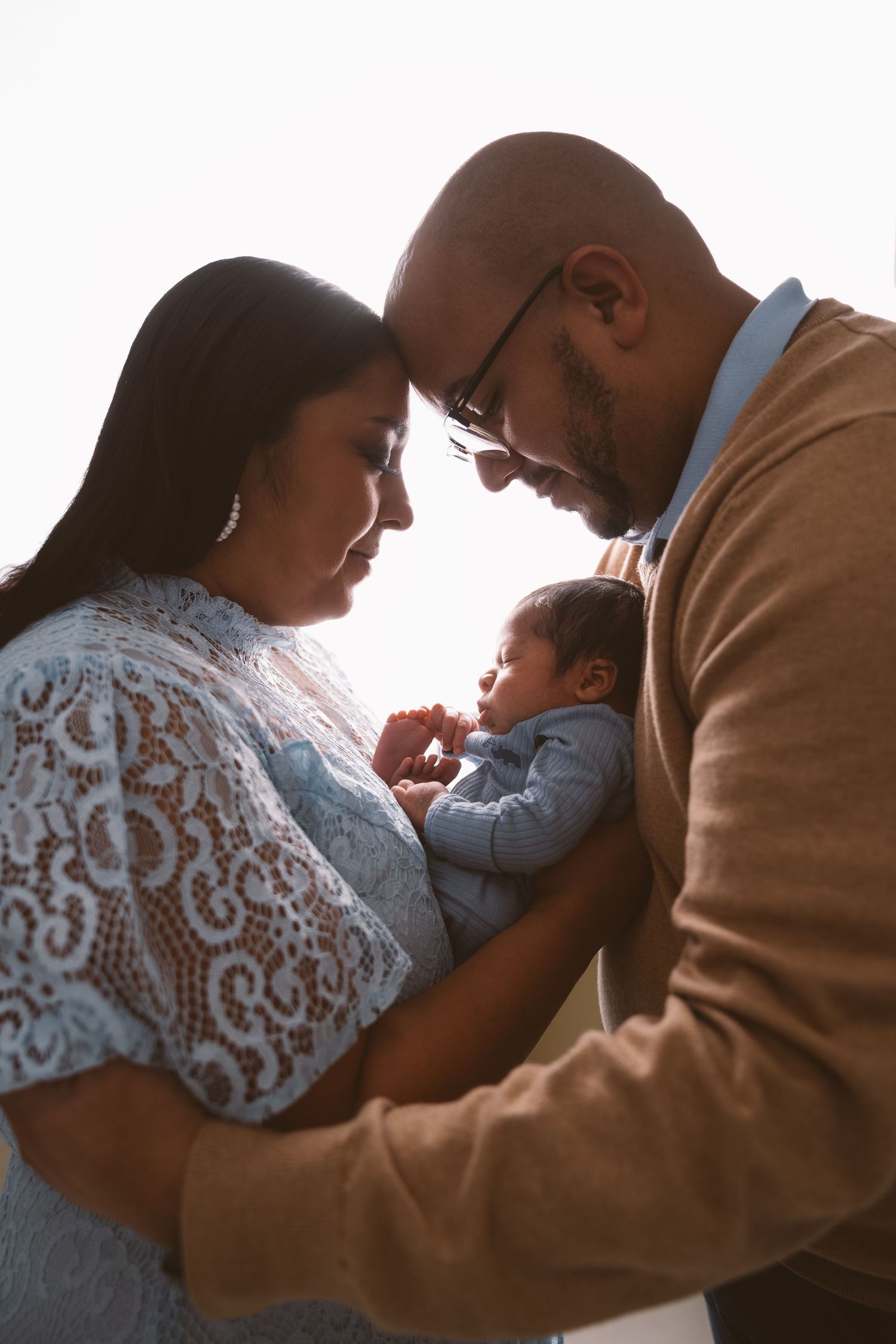 Backlit silhouettes showing tender family moment with newborn baby at sunset.
