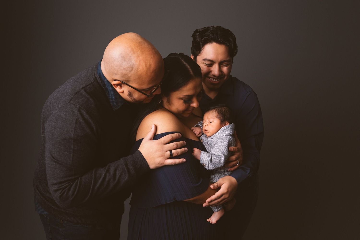Dramatic dark portrait showing intimate family moment with sleeping newborn.