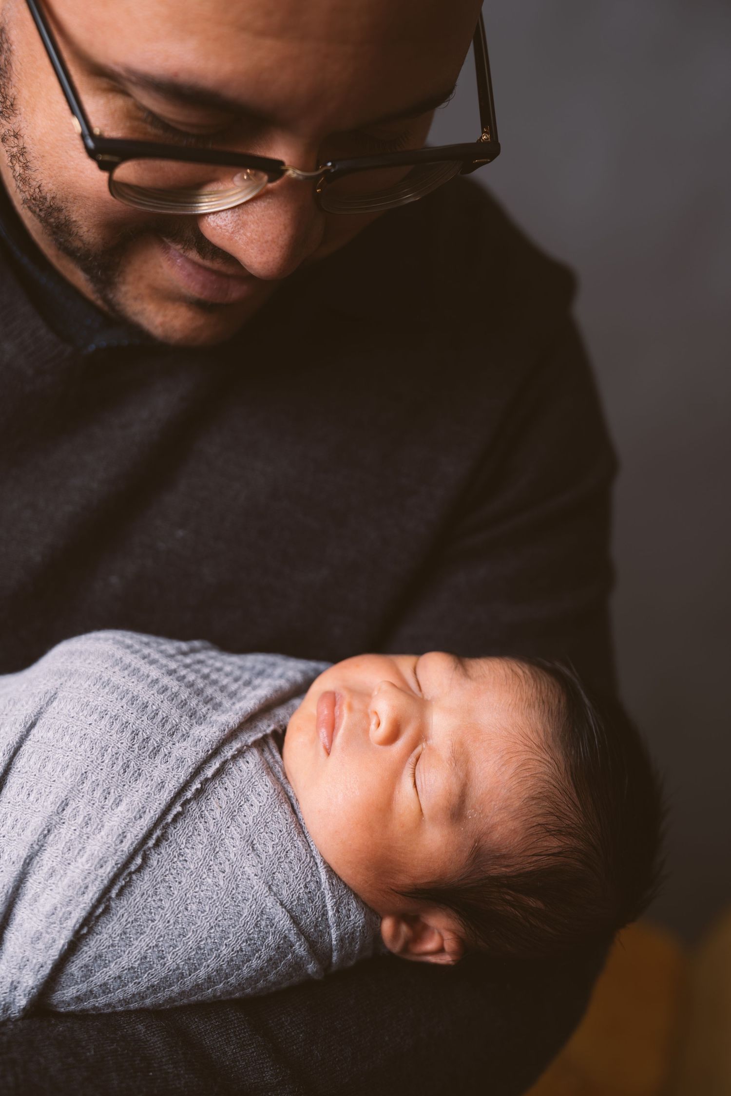 Close-up portrait of sleeping newborn swaddled in gray blanket.