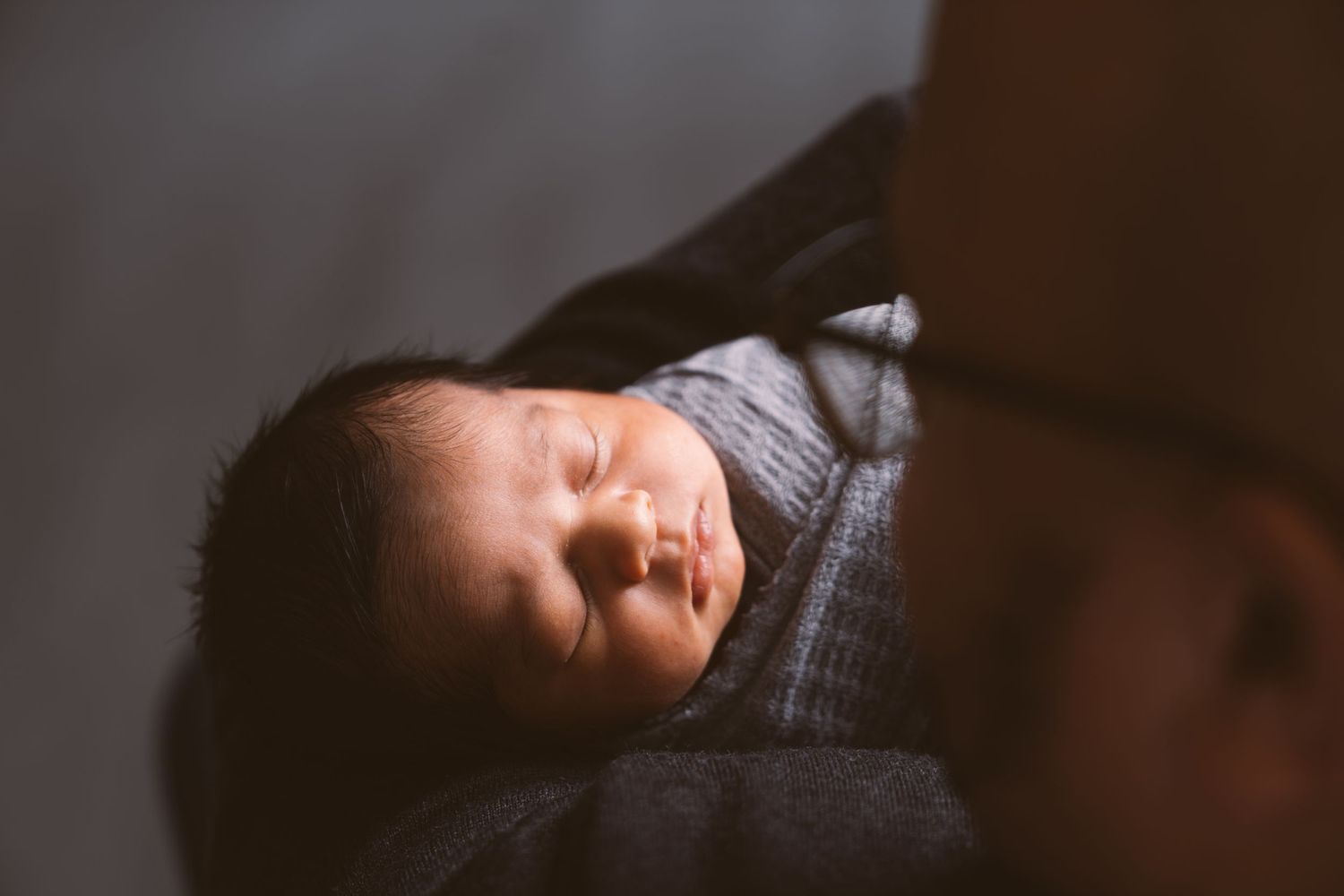 Peaceful newborn baby sleeping while wrapped in soft gray swaddle.
