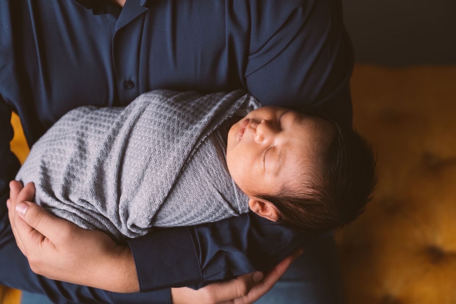 Gentle moment between parent and sleeping newborn in moody lighting.