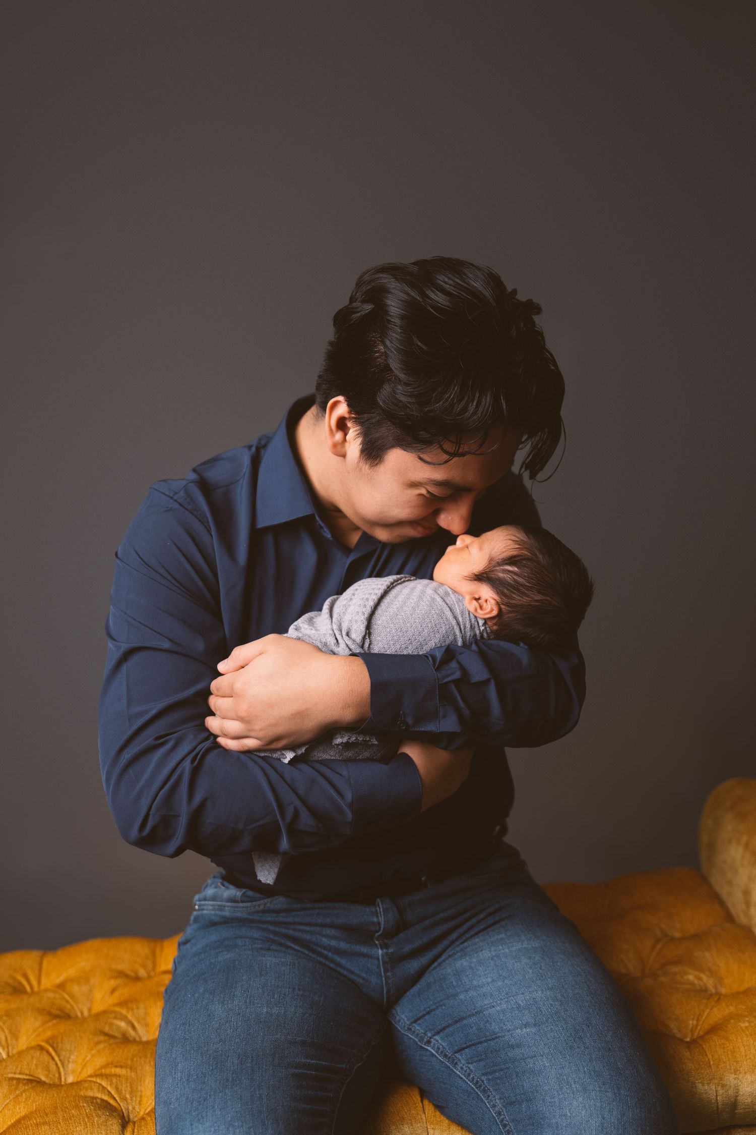 Intimate portrait of parent cradling newborn on yellow tufted couch.