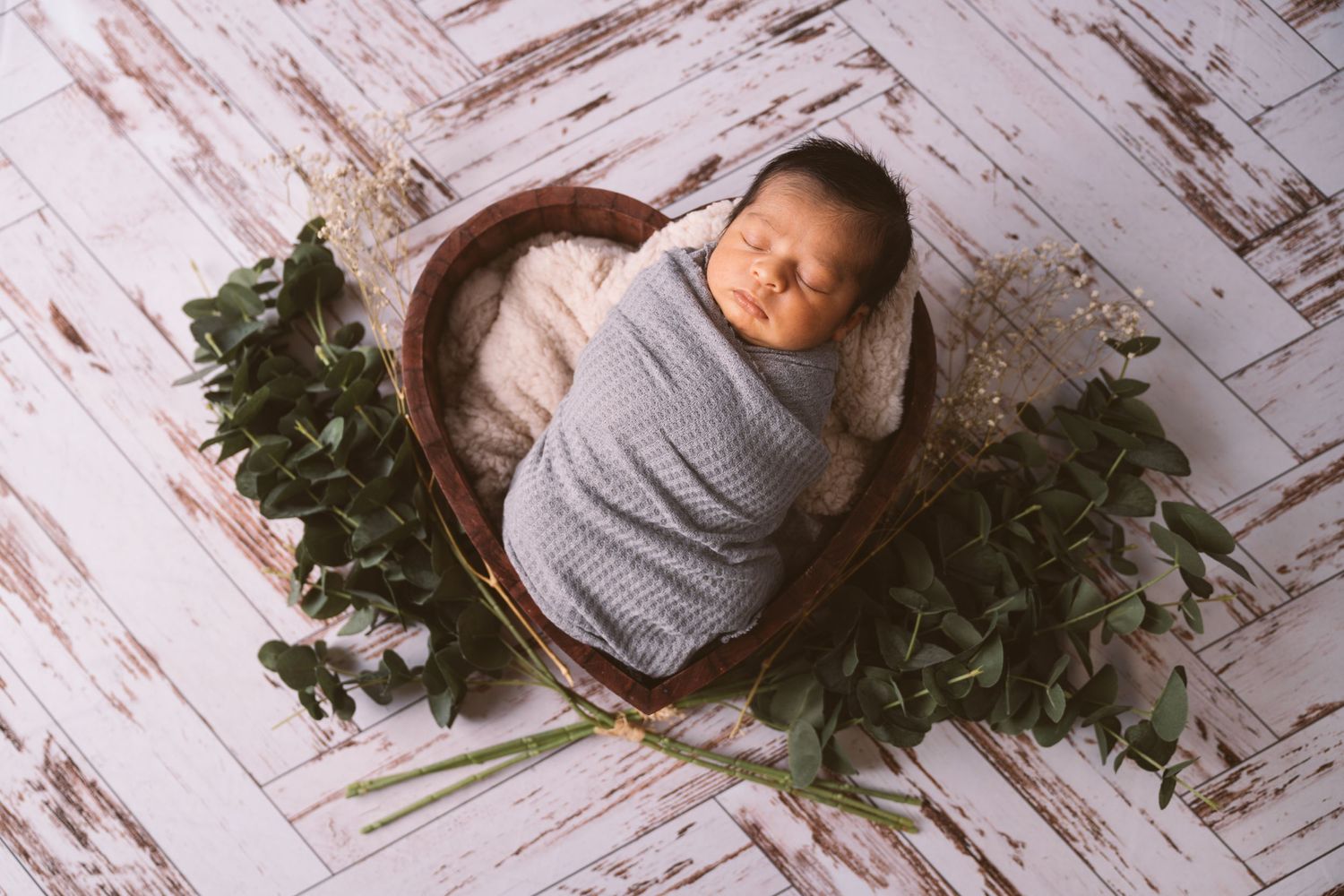 Newborn photography session with baby wrapped in gray against white rustic backdrop.