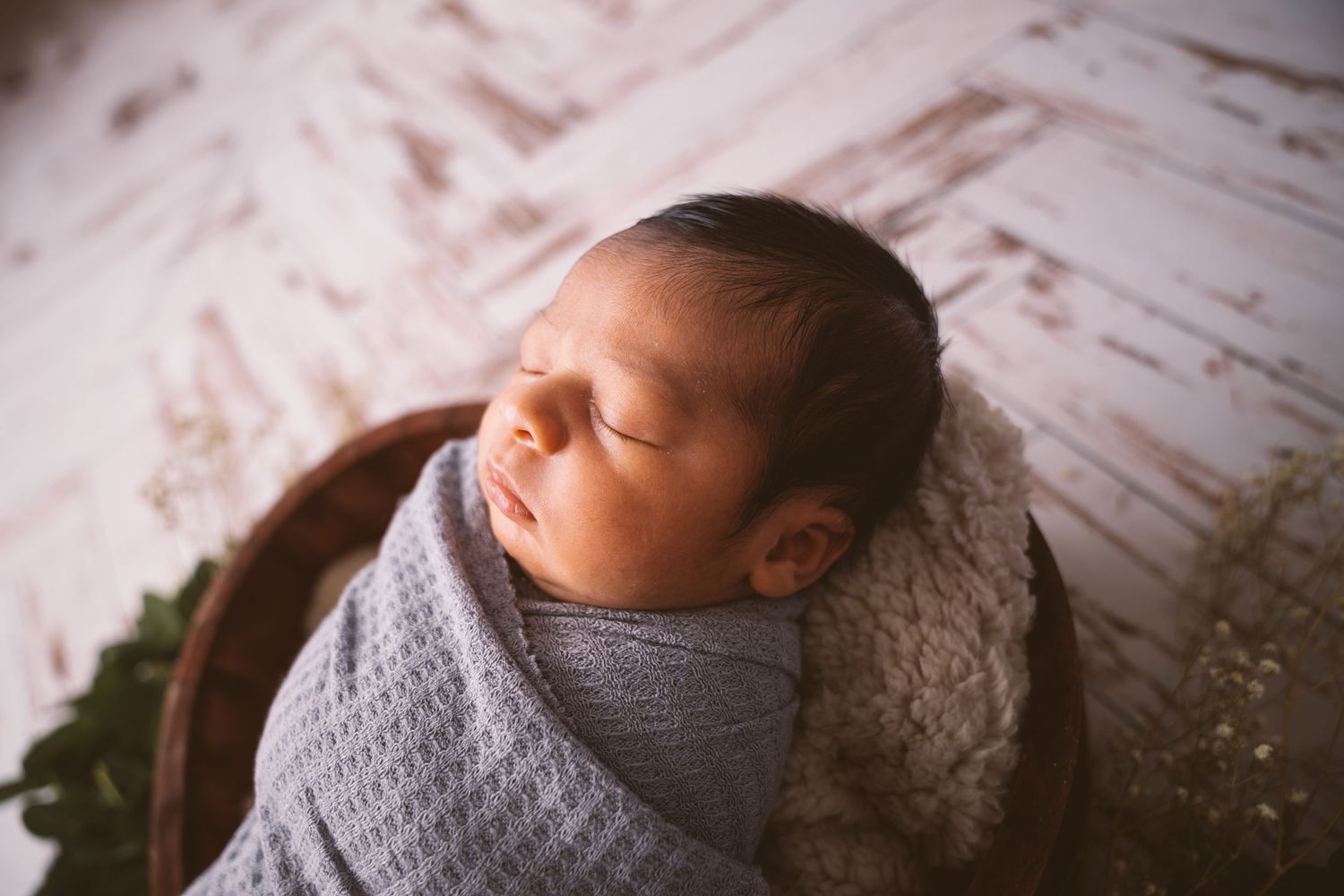 Sleeping newborn wrapped in gray knit blanket during professional photo session.
