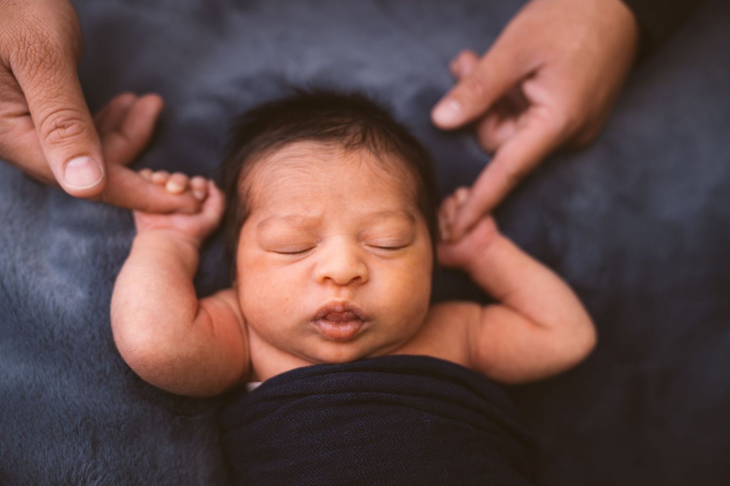 Peaceful sleeping newborn baby lying on dark blue blanket with gentle hands supporting.