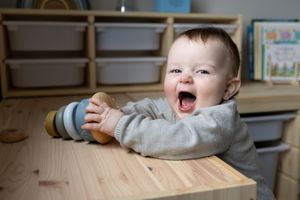 A delighted baby sitting at a wooden table expresses pure joy.