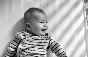 Black and white portrait of a smiling baby wearing a striped shirt.