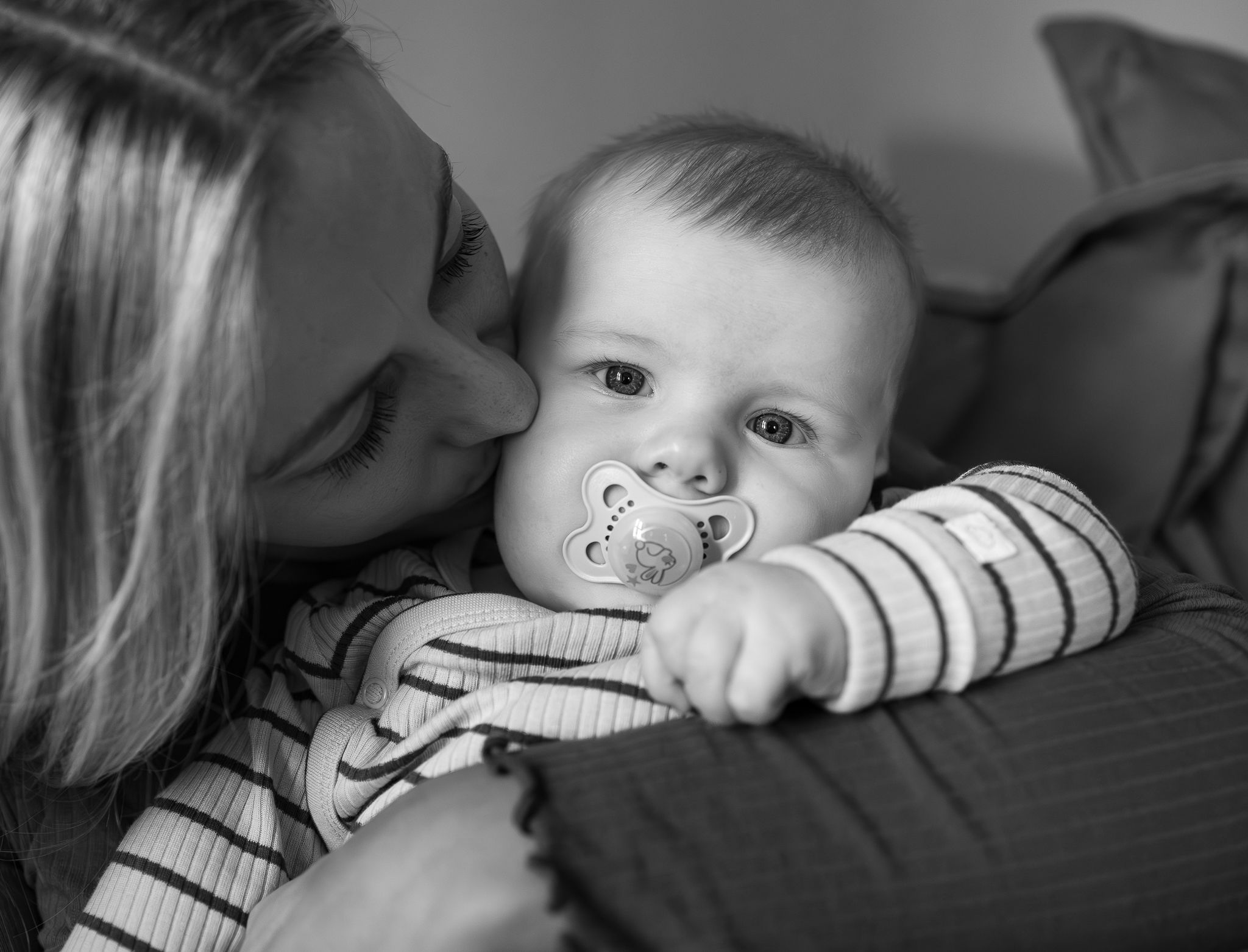 Intimate black and white moment of tender affection with a baby in striped clothing.