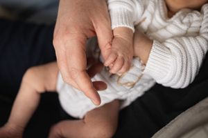 Close up of adult and baby hands touching in white knit clothing.