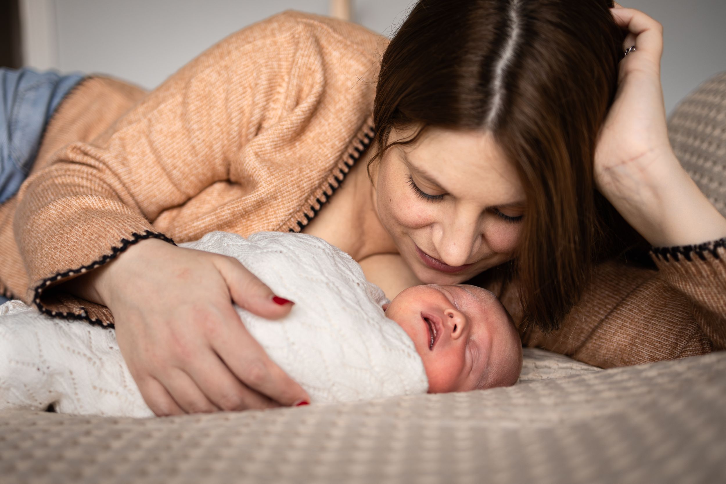 Parent sharing an intimate moment with newborn baby on cozy bedding.