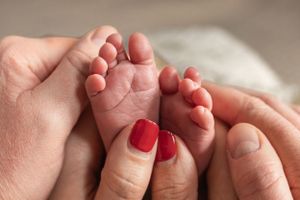 Close up of tiny newborn feet held in adult hands with red nail polish.