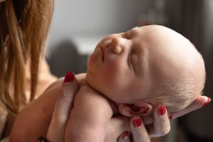 A sleeping newborn lies peacefully in someone's arms with red-painted nails.