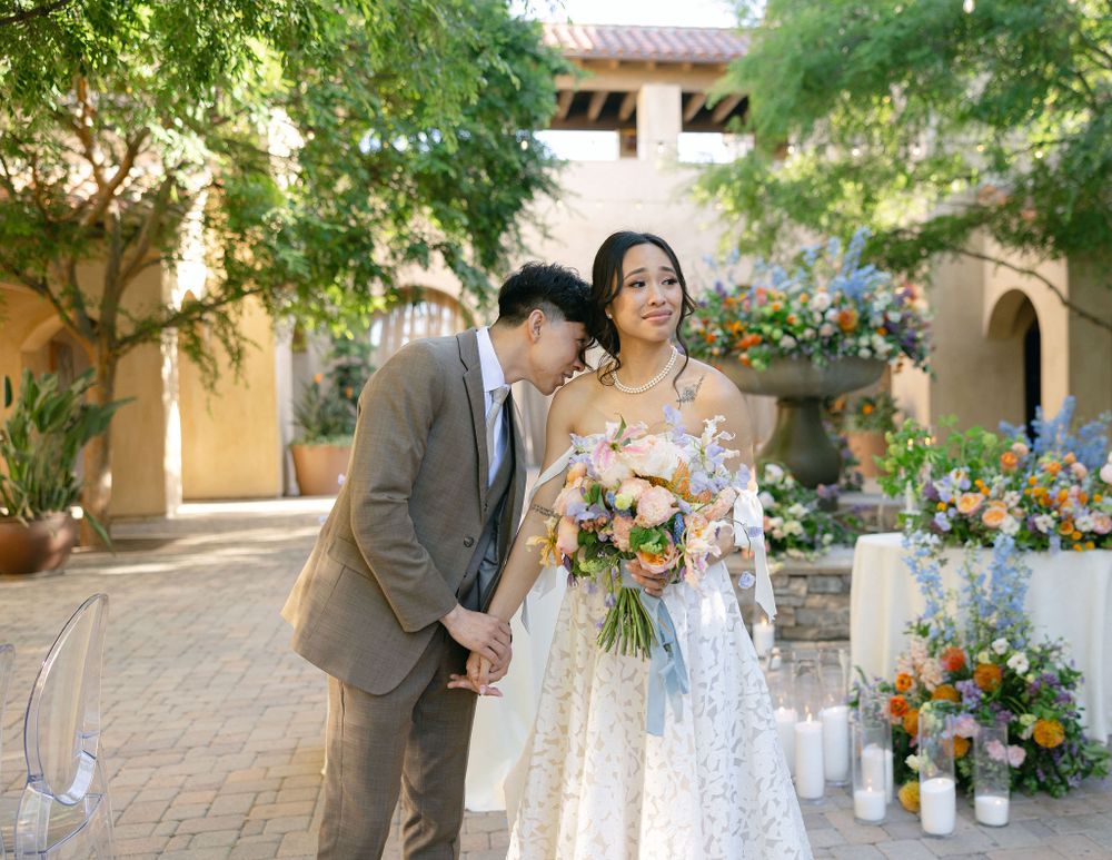 A couple shares a romantic moment in a sunny courtyard decorated with flowers and candles for their wedding ceremony.