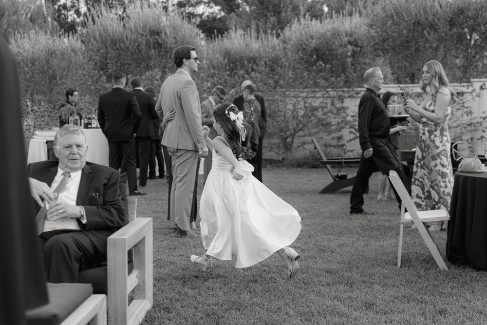 A black and white photograph of an outdoor wedding celebration with guests mingling on a lawn.