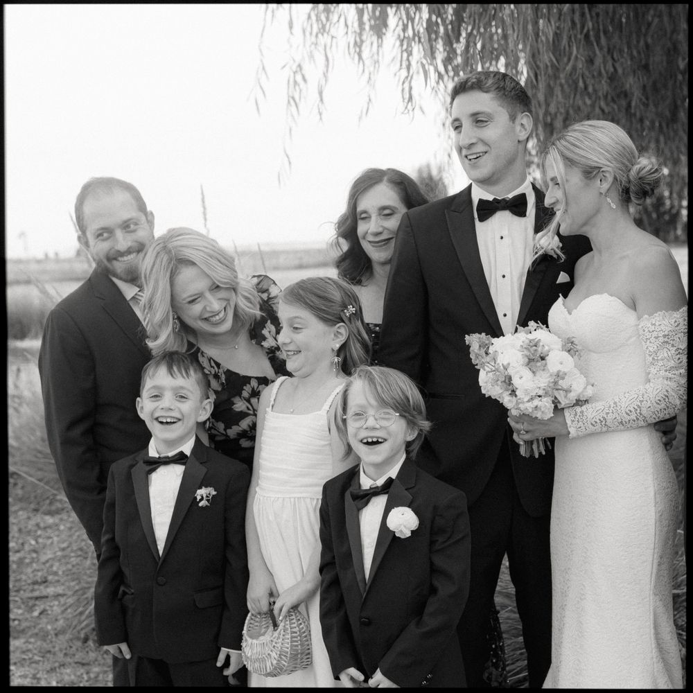 Wedding party members gather under a willow tree for a black and white portrait.