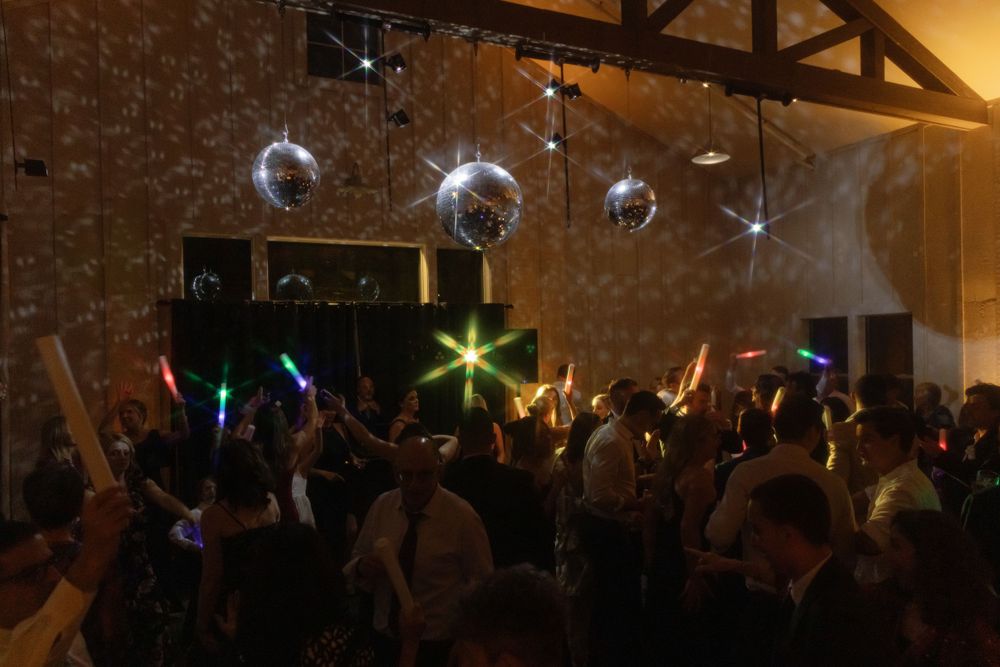 A crowded dance party with disco balls hanging from the ceiling and colorful lights illuminating the dark room.