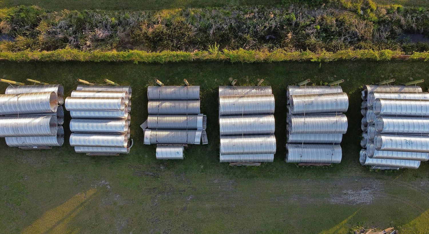 Aerial view of large metal drainage pipes lined up in neat rows.