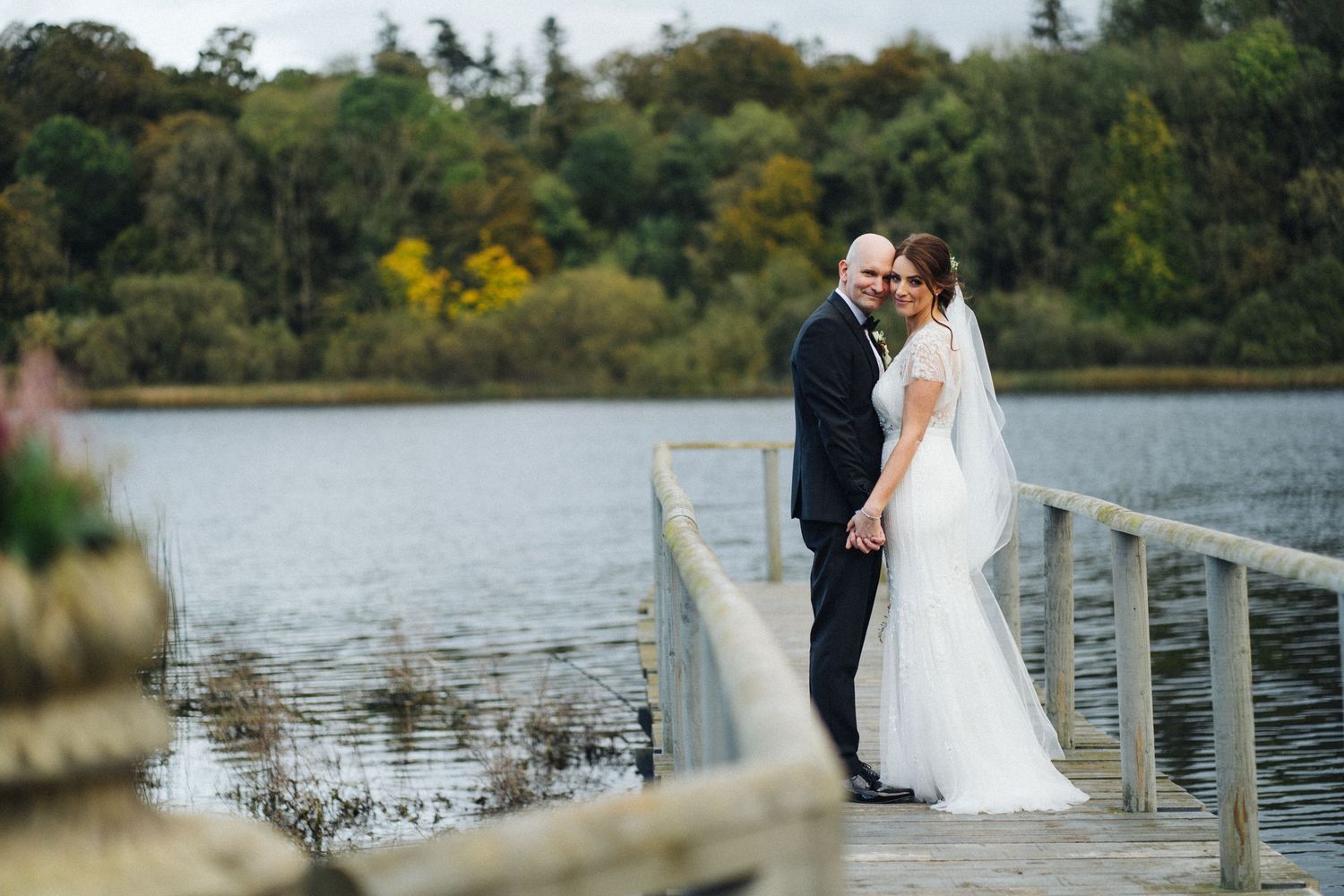 A couple shares a romantic moment on a wooden dock overlooking a serene lake surrounded by autumn trees.