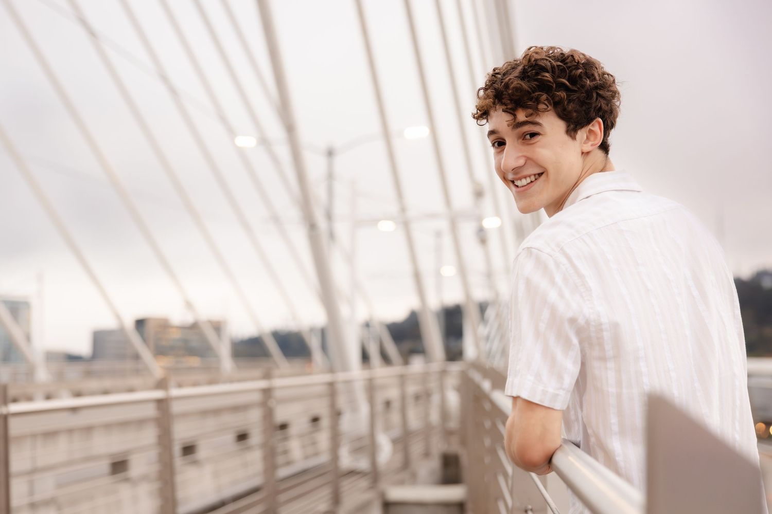 Side view of a person in a white button-down shirt smiling while standing on a bridge.