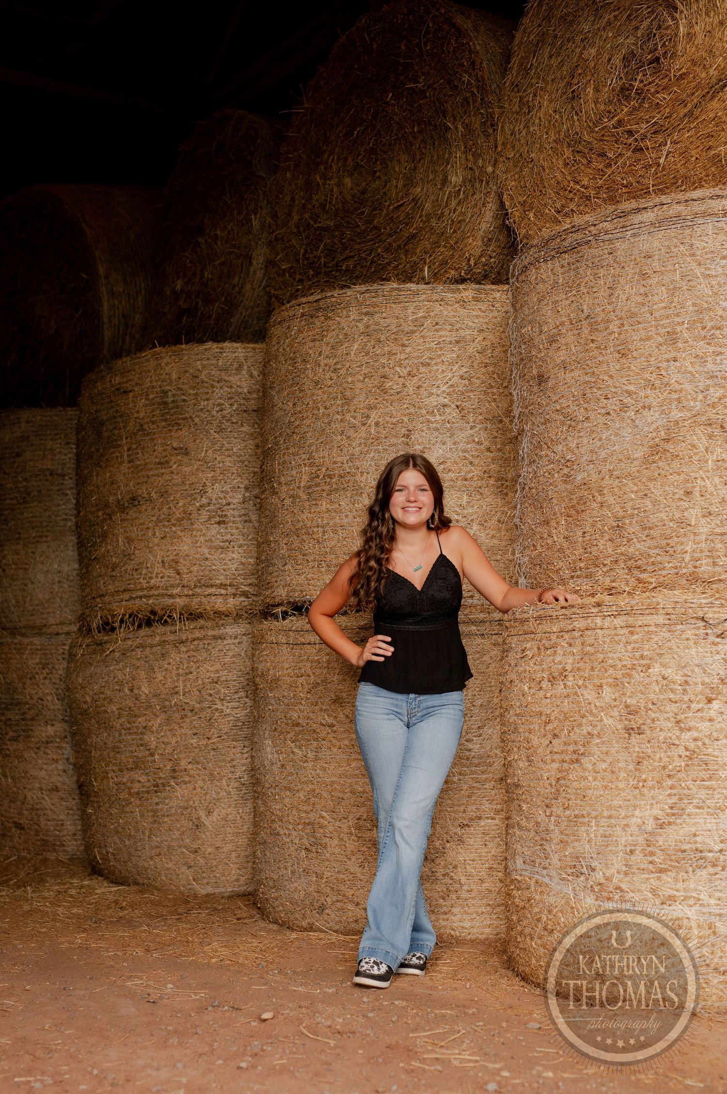 Casual portrait leaning against stacked hay bales in barn setting.