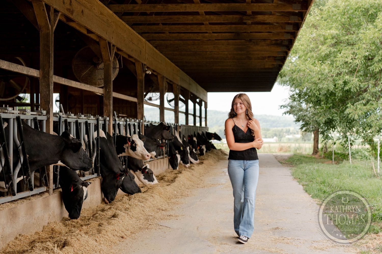 Black tank top and jeans outfit walking along barn path with Holstein cows in stalls.