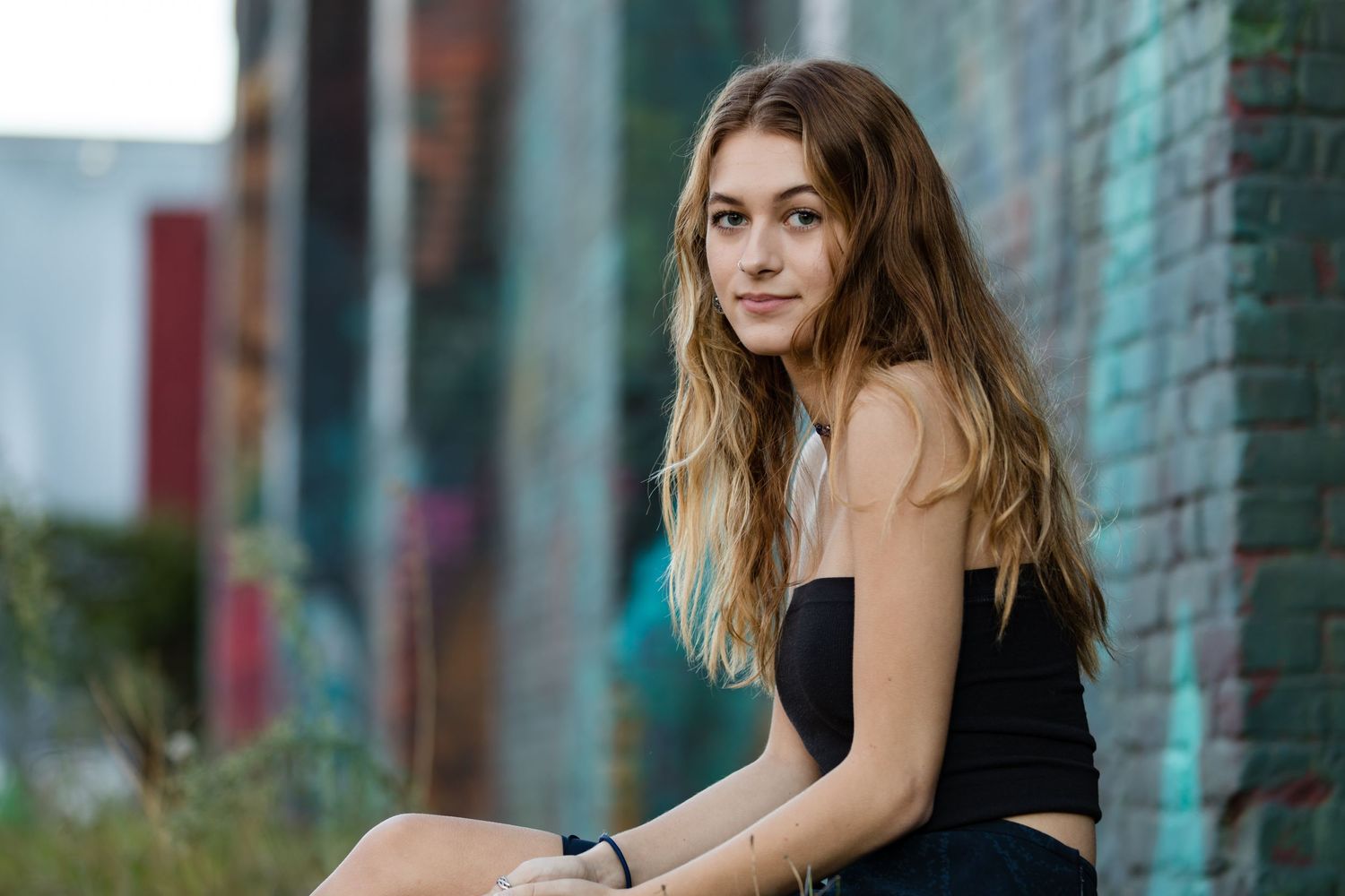 A casual outdoor portrait in an urban setting with a black top against a teal and brick wall background.