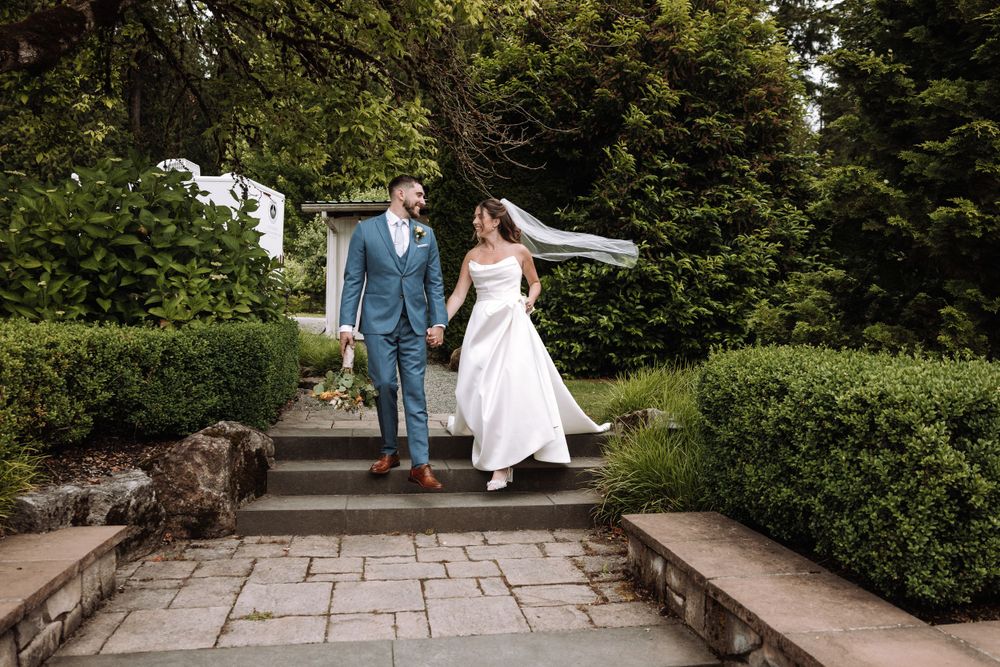 A couple descends stone steps through a manicured garden on their wedding day.
